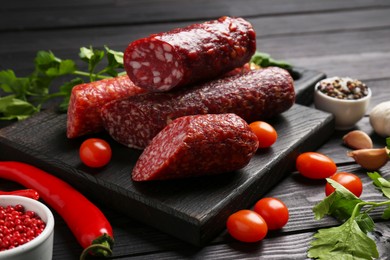 Photo of Different smoked sausages, tomatoes and chili pepper on black wooden table, closeup