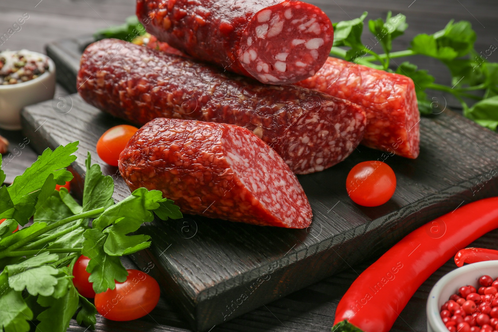 Photo of Different smoked sausages, tomatoes and chili pepper on black wooden table, closeup