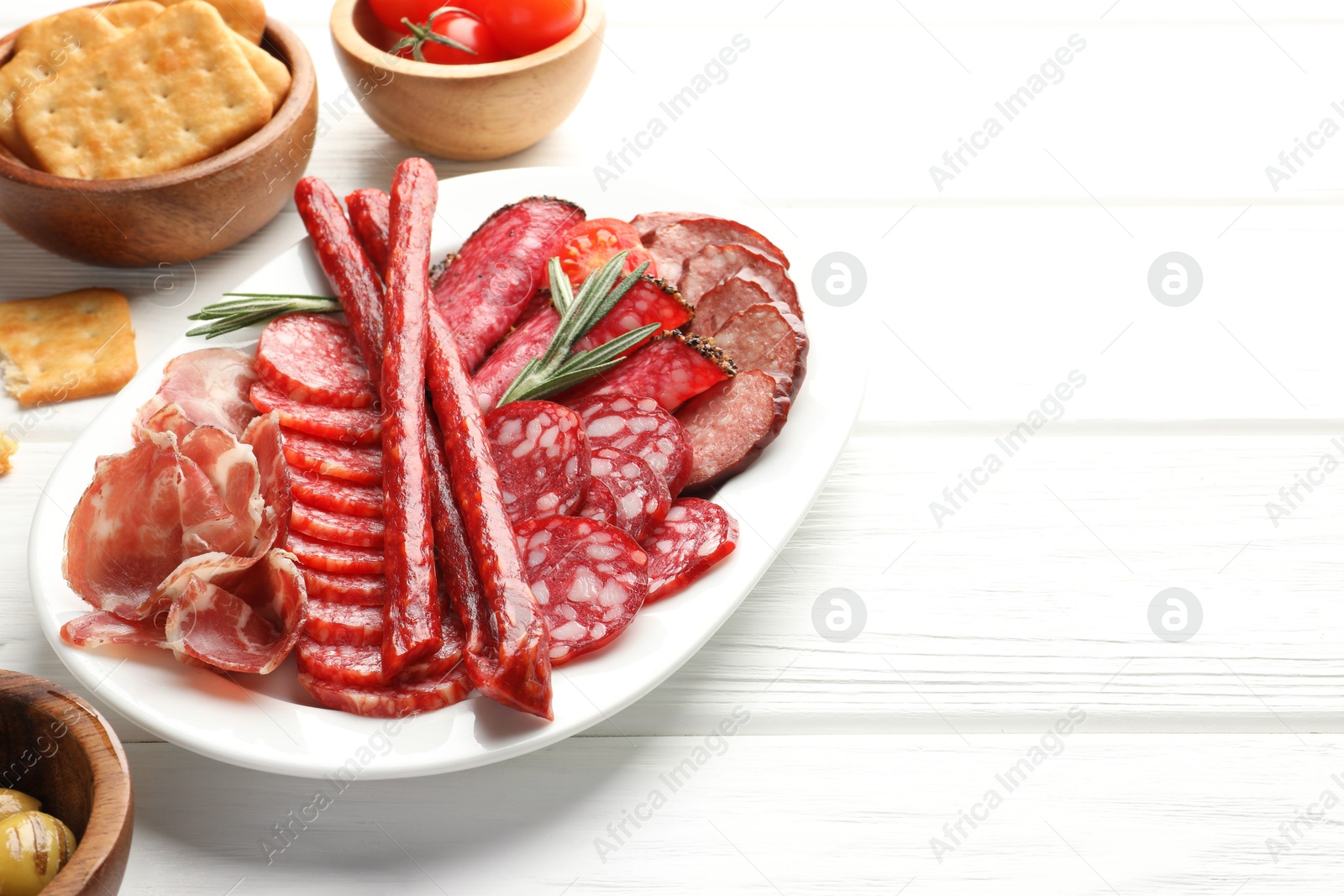 Photo of Different smoked sausages slices served on white wooden table, closeup. Space for text