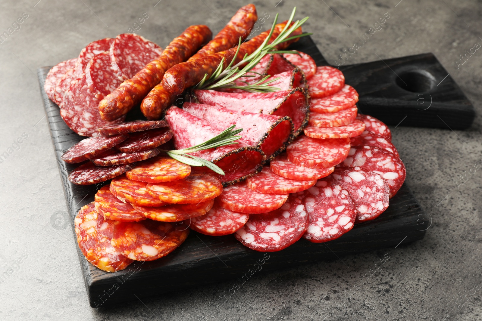 Photo of Different smoked sausages slices served on grey table, closeup