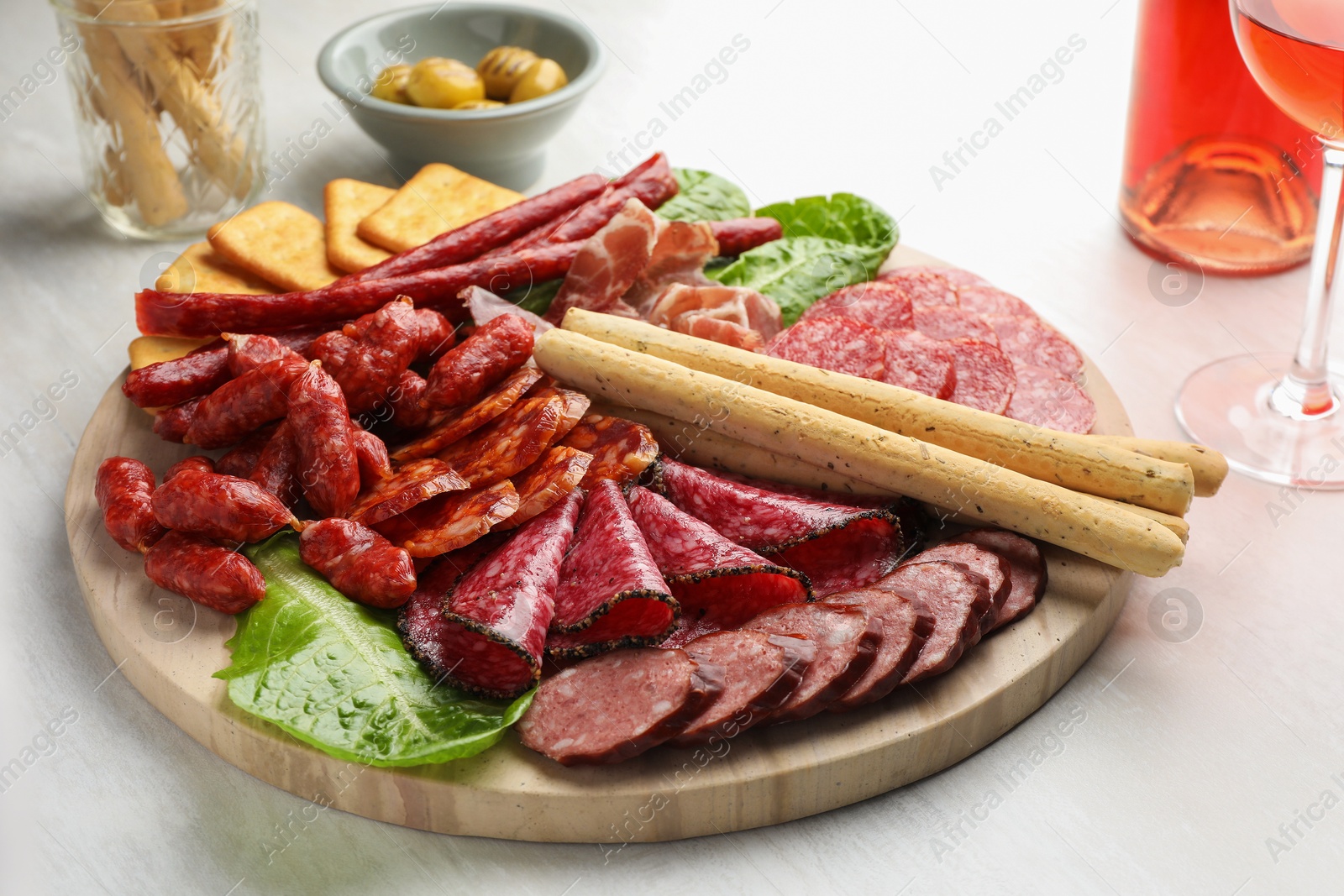 Photo of Different smoked sausages and other snacks served with wine on white table, closeup