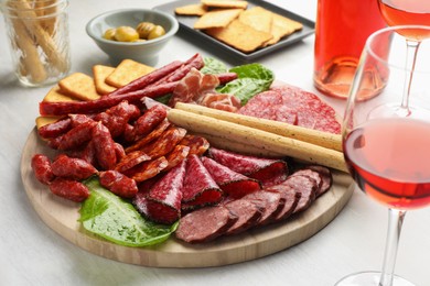 Photo of Different smoked sausages and other snacks served with wine on white table, closeup