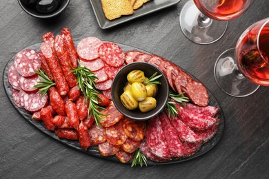 Photo of Different smoked sausages and other snacks served with wine on black table, flat lay