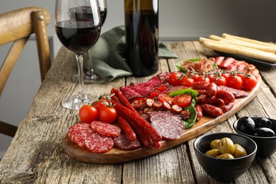 Photo of Different smoked sausages and other snacks served with wine on wooden table, closeup