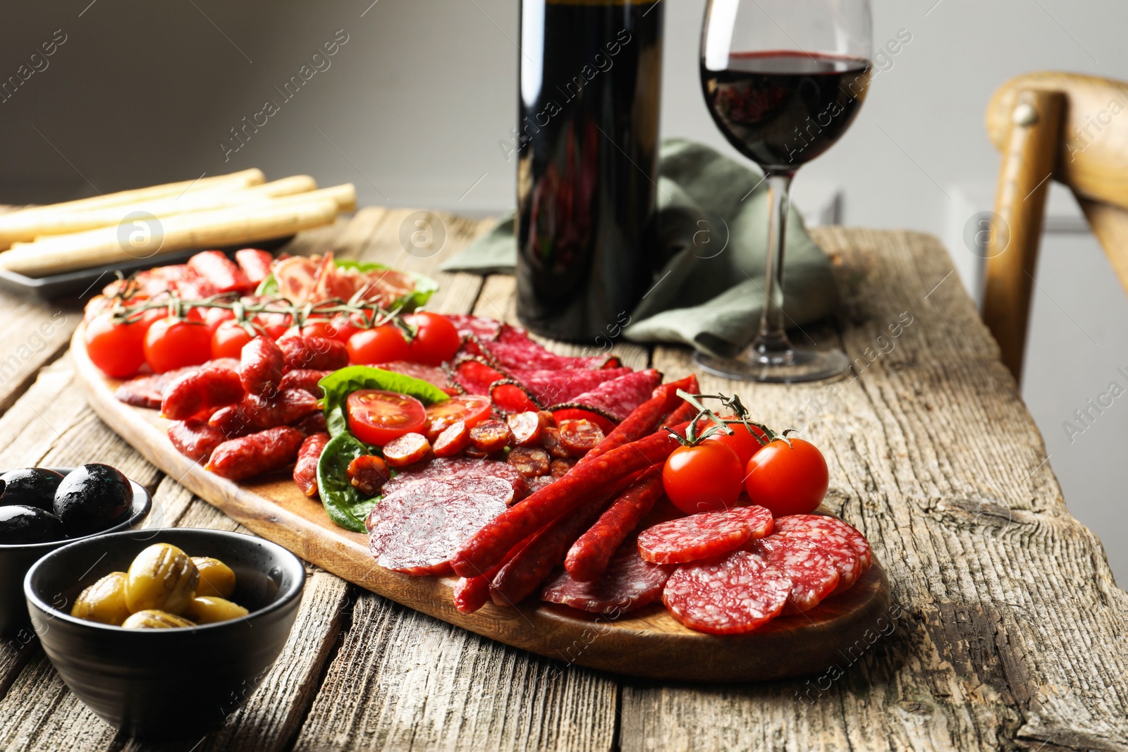 Photo of Different smoked sausages and other snacks served with wine on wooden table, closeup