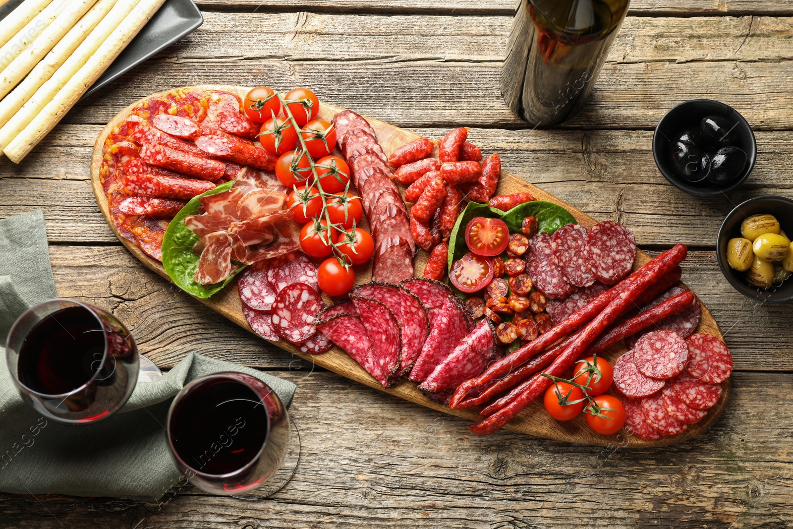 Photo of Different smoked sausages and other snacks served with wine on wooden table, flat lay