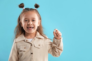 Photo of Cute little girl with missing tooth on light blue background, space for text. Waiting for tooth fairy