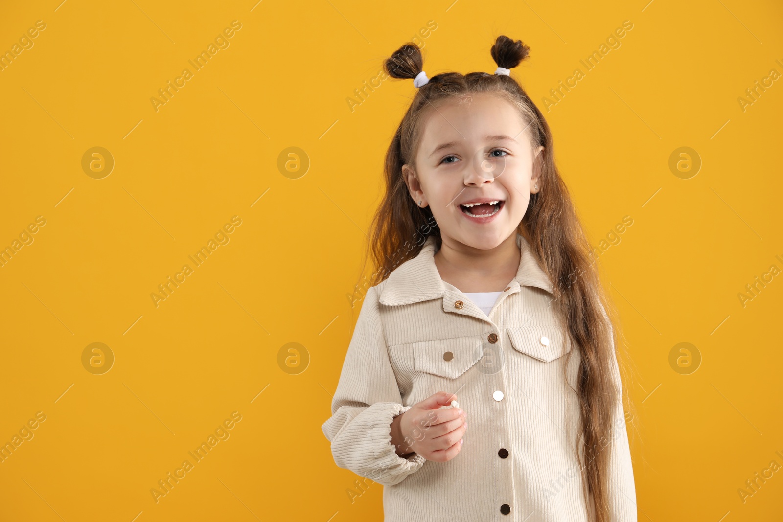 Photo of Cute little girl with missing tooth on orange background, space for text. Waiting for tooth fairy