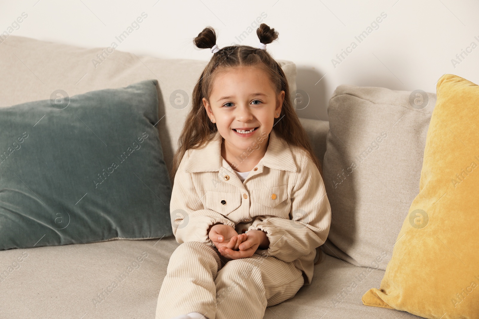 Photo of Cute little girl with missing tooth on sofa indoors. Waiting for tooth fairy