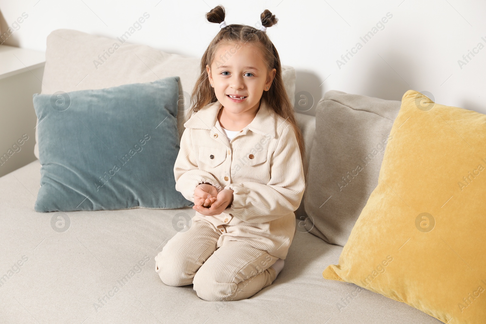 Photo of Cute little girl with missing tooth on sofa indoors. Waiting for tooth fairy