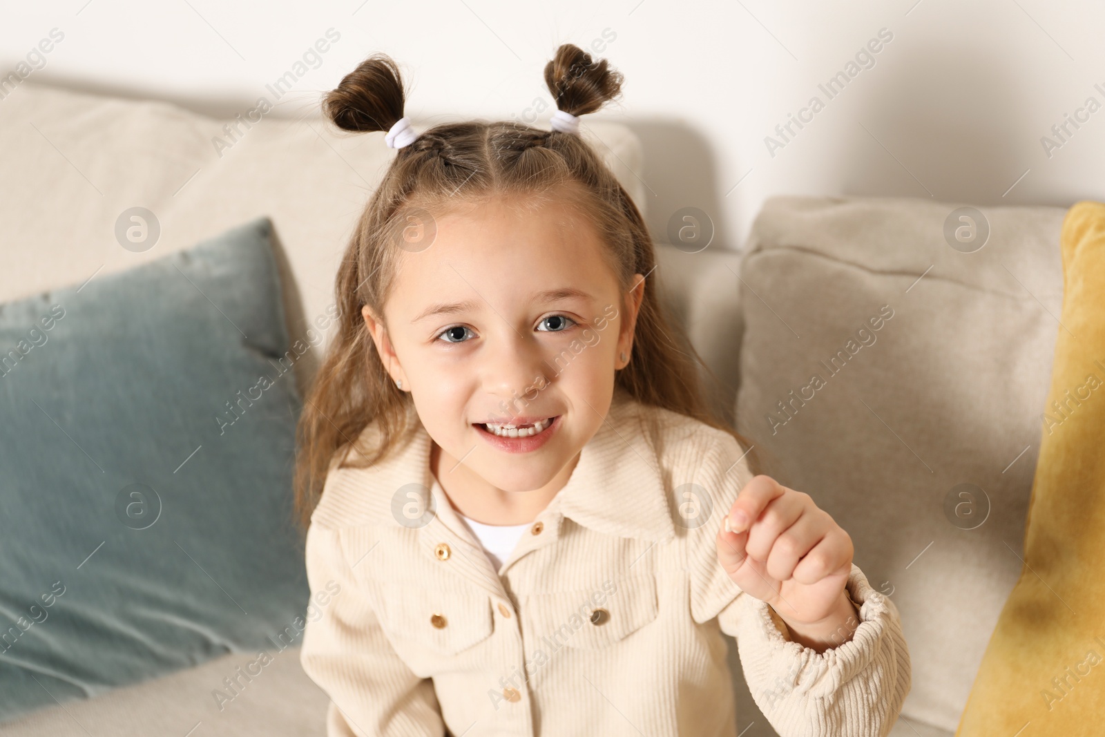 Photo of Cute little girl with missing tooth on sofa indoors. Waiting for tooth fairy