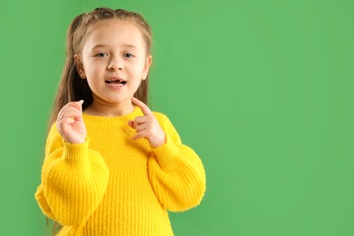 Photo of Cute little girl with missing tooth on green background, space for text. Waiting for tooth fairy