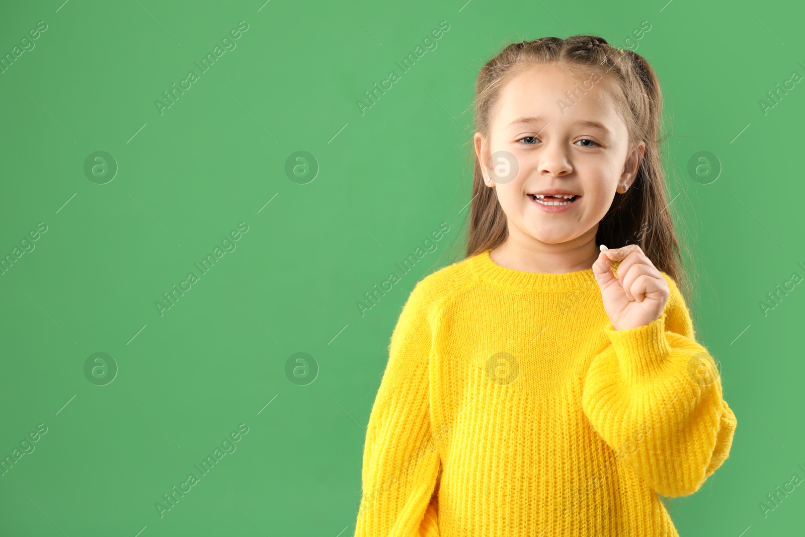 Photo of Cute little girl with missing tooth on green background, space for text. Waiting for tooth fairy