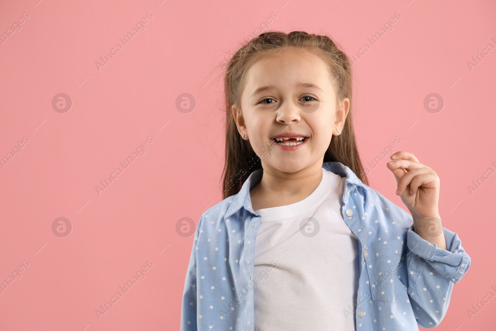 Photo of Portrait of cute little girl with missing tooth on pink background, space for text