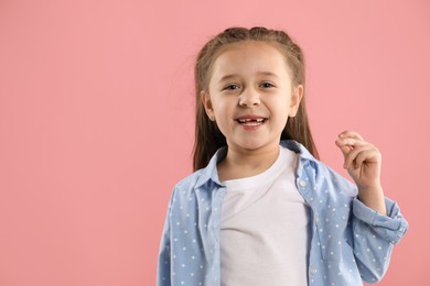 Photo of Portrait of cute little girl with missing tooth on pink background, space for text