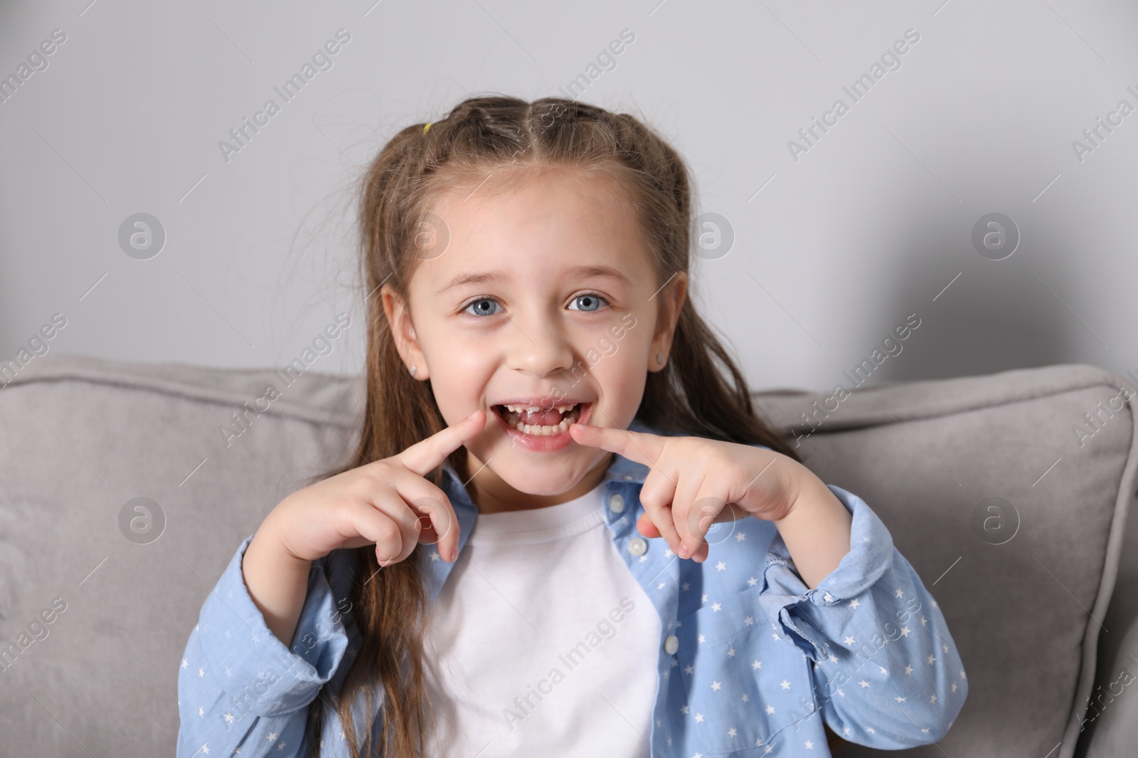 Photo of Cute little girl pointing at her missing tooth in armchair. Waiting for tooth fairy