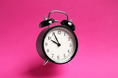 Photo of Black alarm clock in air on bright pink background