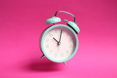 Photo of Turquoise alarm clock in air on bright pink background