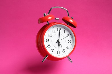 Photo of Red alarm clock in air on bright pink background
