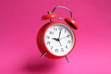 Photo of Red alarm clock in air on bright pink background