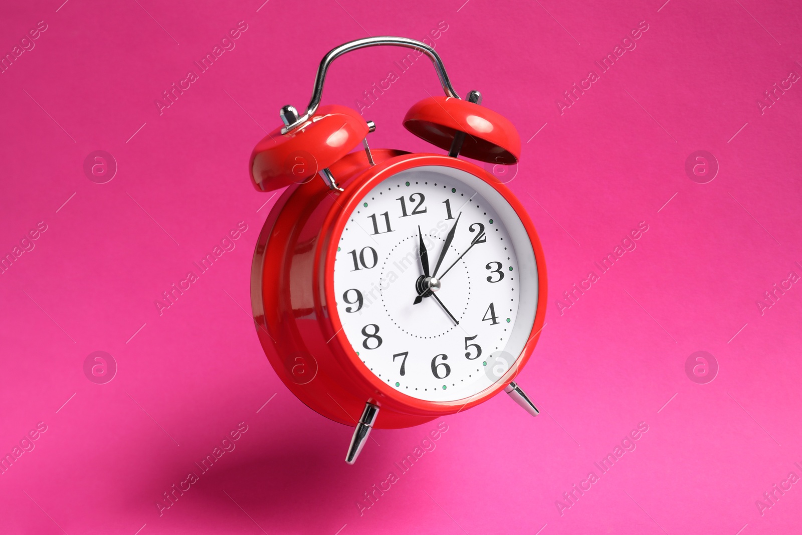 Photo of Red alarm clock in air on bright pink background