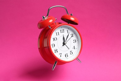 Photo of Red alarm clock in air on bright pink background