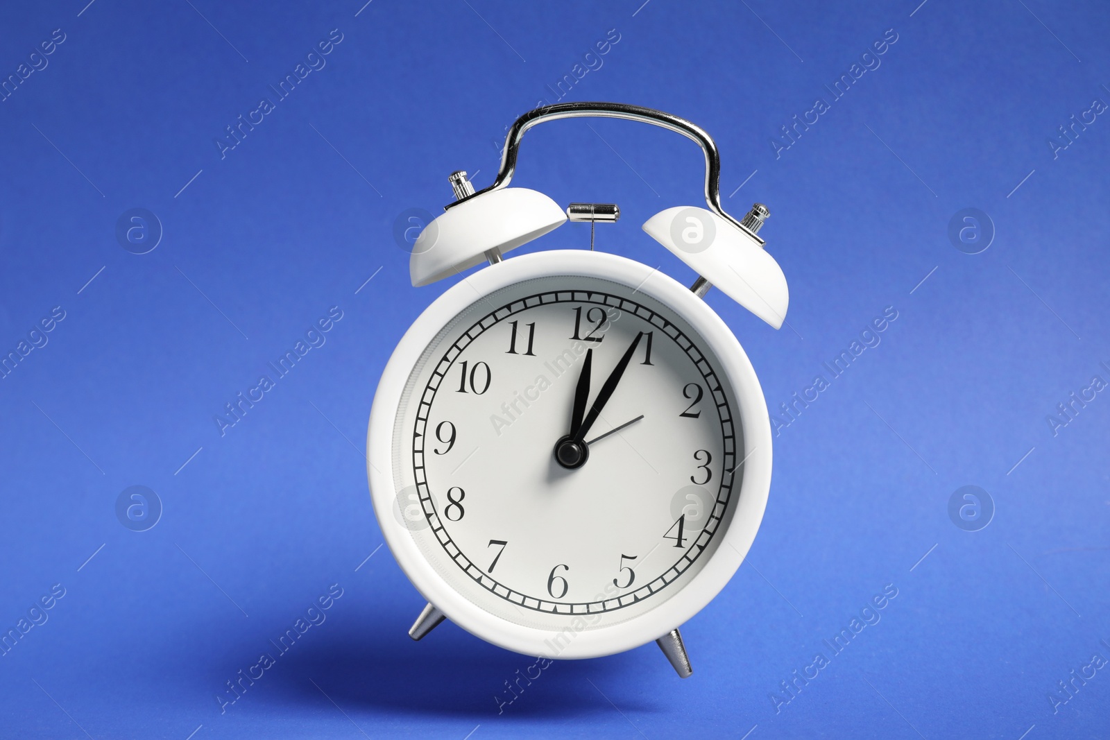 Photo of White alarm clock in air on blue background