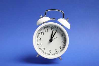 Photo of White alarm clock in air on blue background