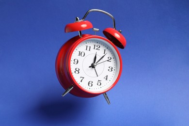 Photo of Red alarm clock in air on blue background