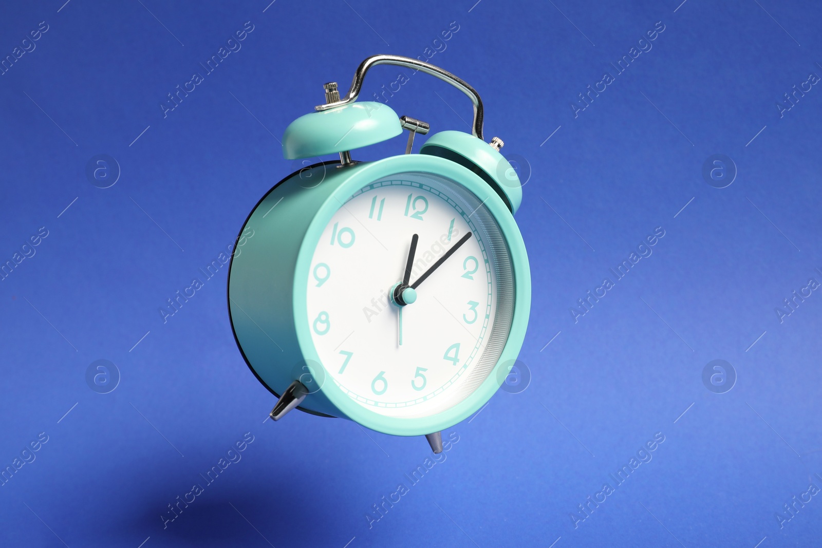 Photo of Turquoise alarm clock in air on blue background