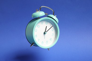 Photo of Turquoise alarm clock in air on blue background