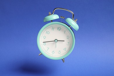 Photo of Turquoise alarm clock in air on blue background