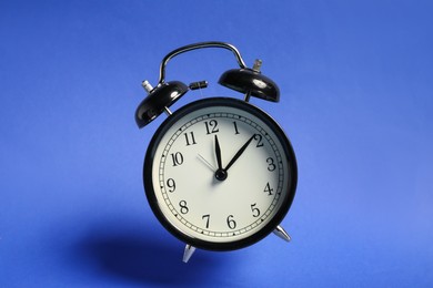Photo of Black alarm clock in air on blue background