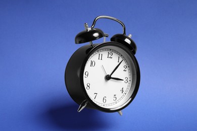 Photo of Black alarm clock in air on blue background