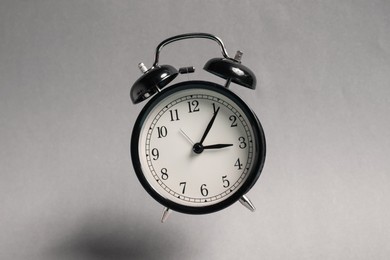 Photo of Black alarm clock in air on light grey background