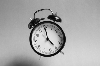 Photo of Black alarm clock in air on light grey background