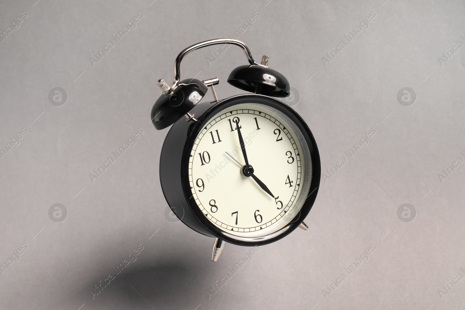 Photo of Black alarm clock in air on light grey background