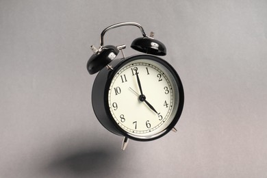 Photo of Black alarm clock in air on light grey background