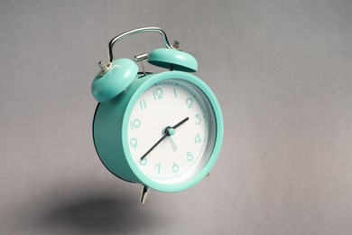 Photo of Turquoise alarm clock in air on light grey background