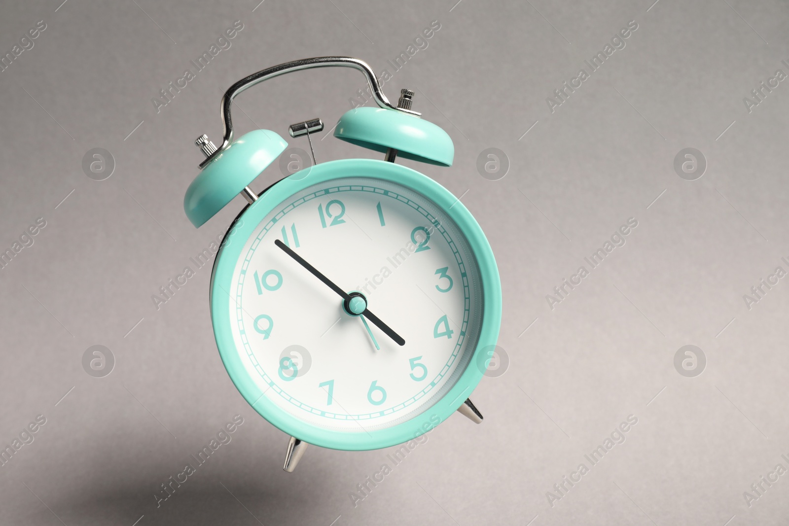Photo of Turquoise alarm clock in air on light grey background
