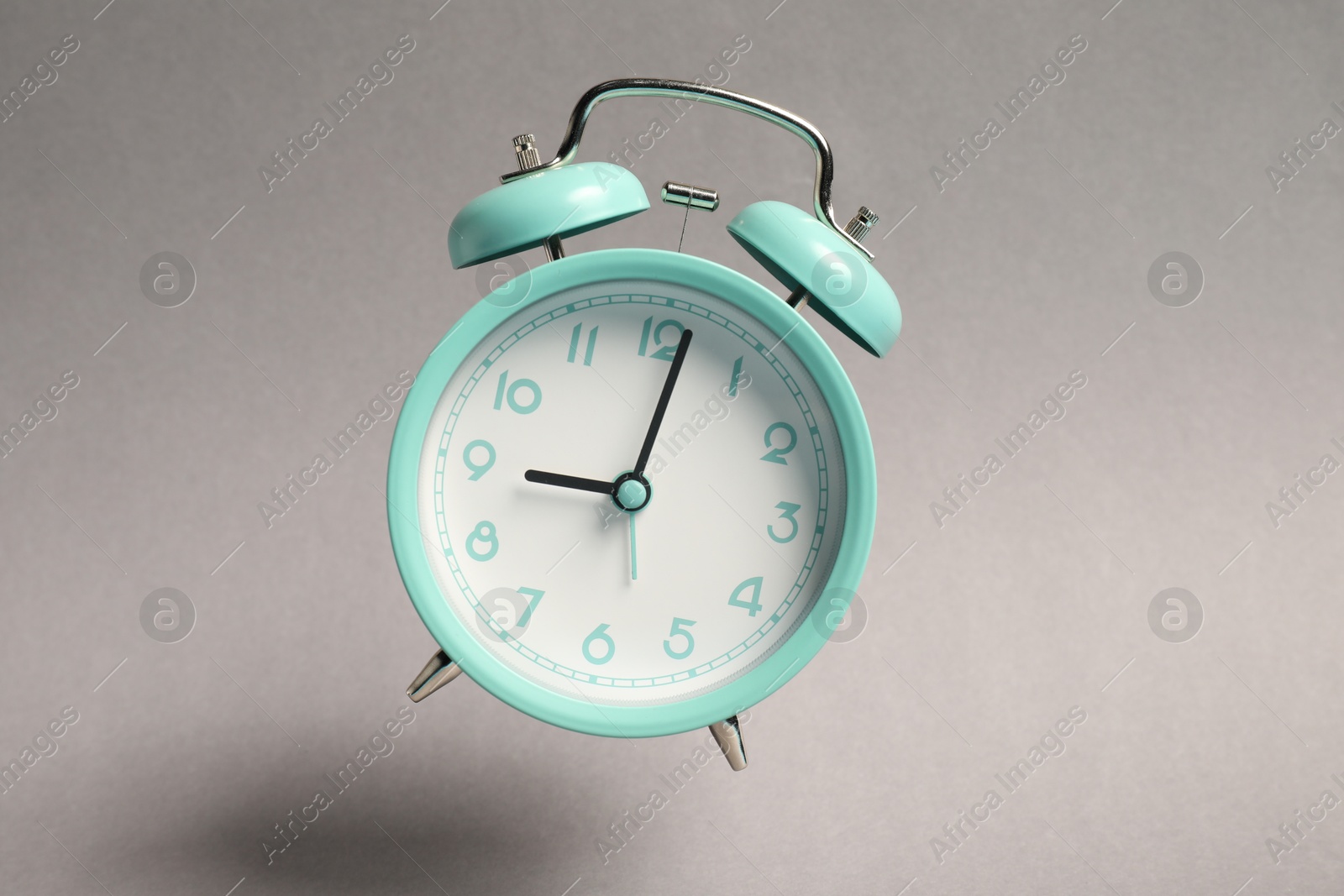 Photo of Turquoise alarm clock in air on light grey background