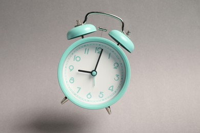 Photo of Turquoise alarm clock in air on light grey background
