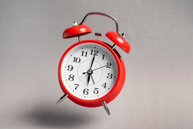 Photo of Red alarm clock in air on light grey background