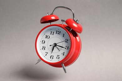 Photo of Red alarm clock in air on light grey background
