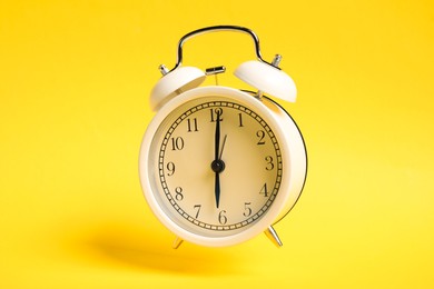 Photo of White alarm clock in air on yellow background