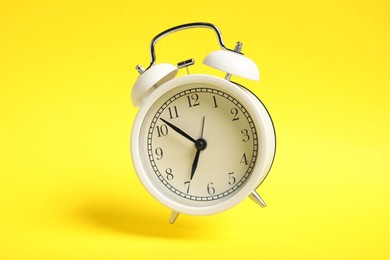 Photo of White alarm clock in air on yellow background