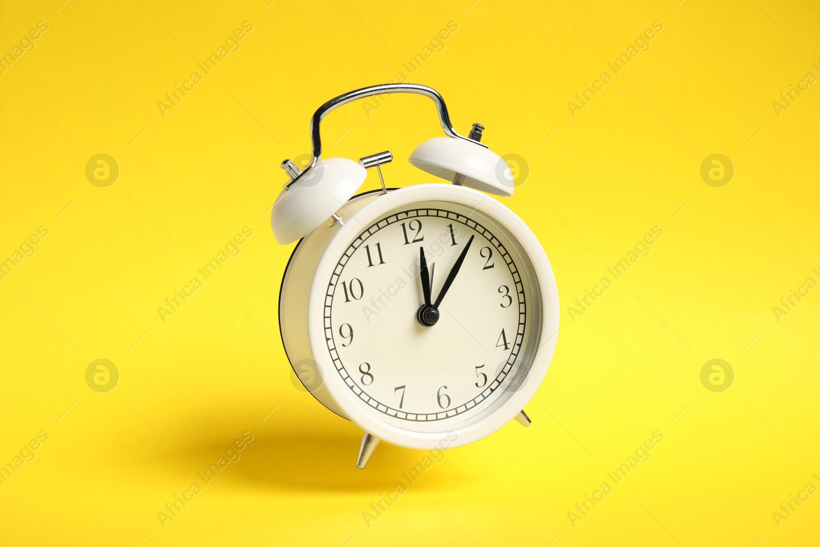 Photo of White alarm clock in air on yellow background