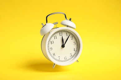 Photo of White alarm clock in air on yellow background
