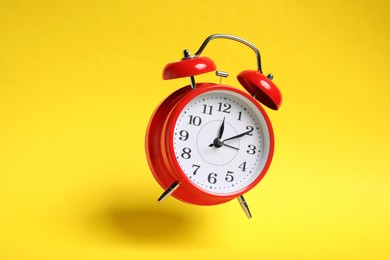 Photo of Red alarm clock in air on yellow background