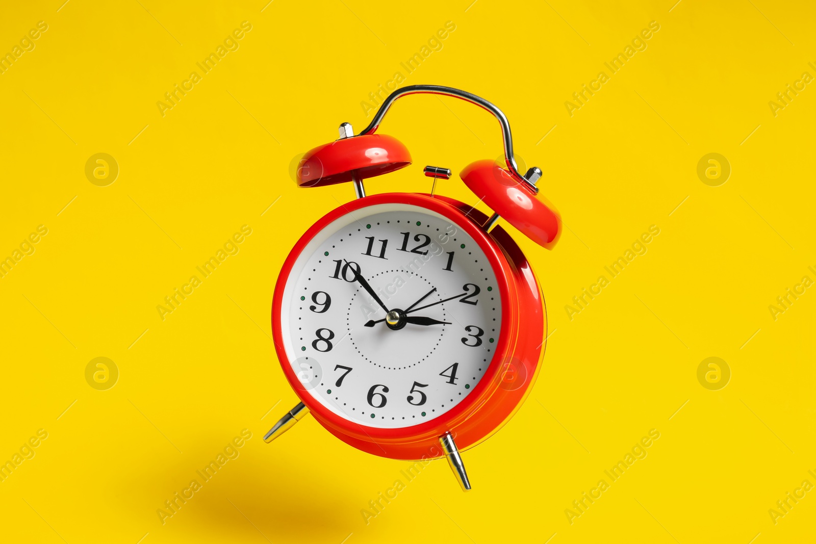 Photo of Red alarm clock in air on yellow background